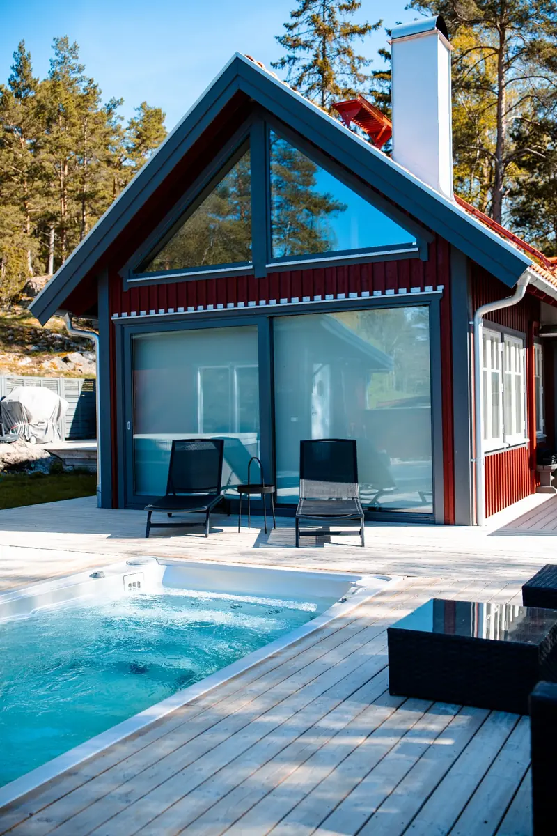 USSPA swimspa nedsänkt i trädäck framför ett rött hus en sommardag