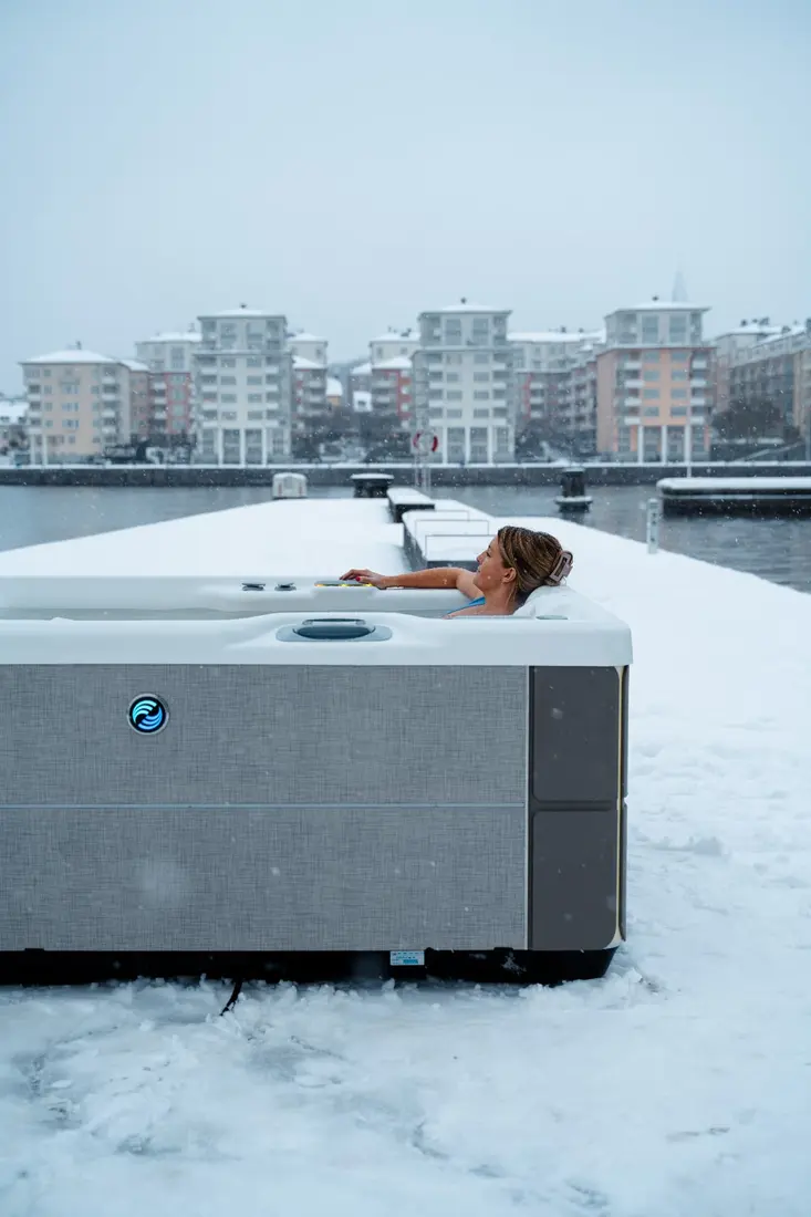 Kvinna lutar sig tillbaka i ett HotSpring Highlife spabad på en snöig brygga