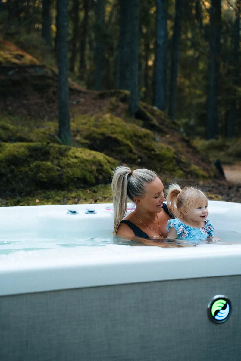 Mamma och liten dotter badar i ett HotSpring spabad med höstskog bakom