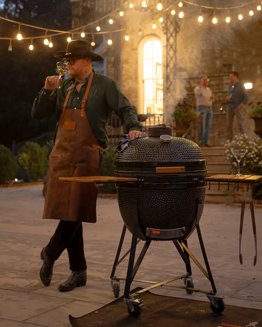 Grillmästare i förkläde vid en KAMADO SUMO Maxi under ljusslingor på en grillkväll