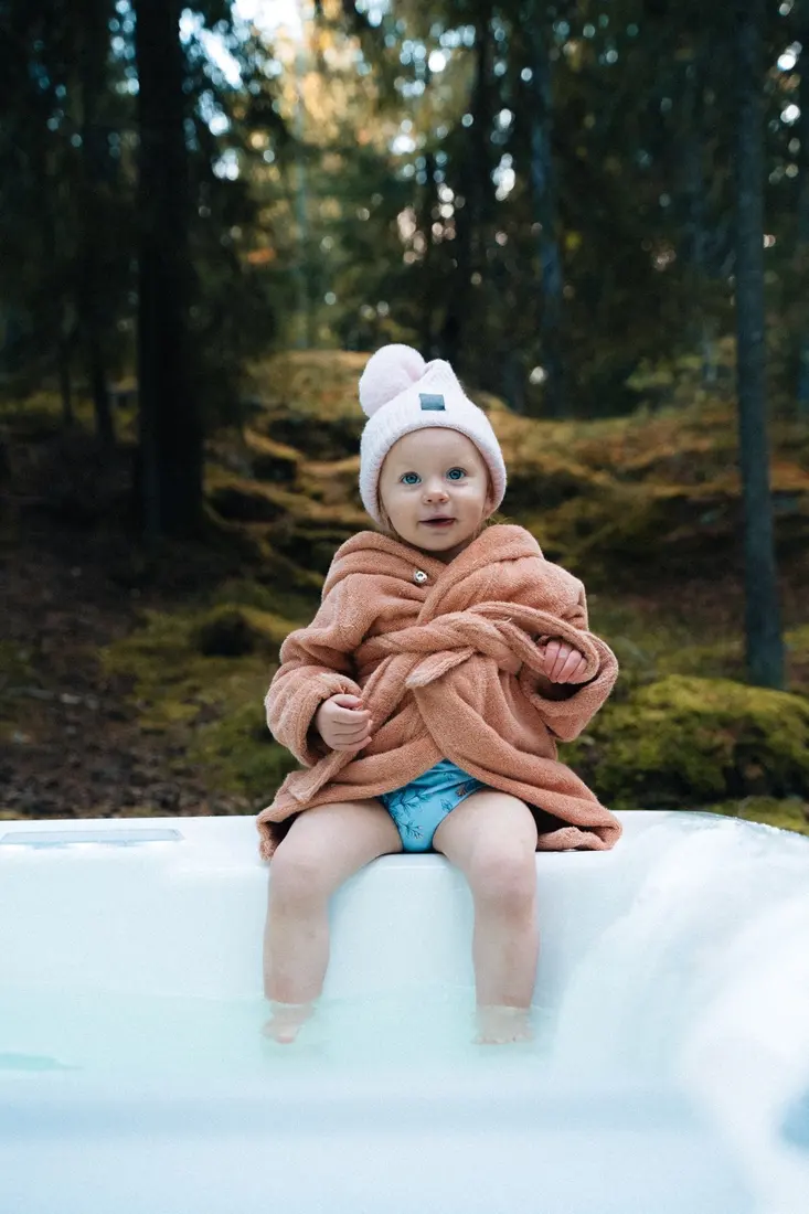 Barn i badrock sitter på kanten av ett HotSpring spabad en höstdag
