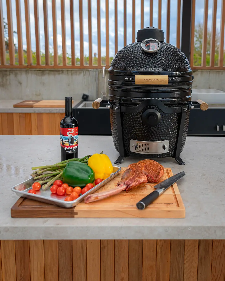 KAMADO SUMO Junior i ett utekök med grönsaker och tomahawksteak på bänken