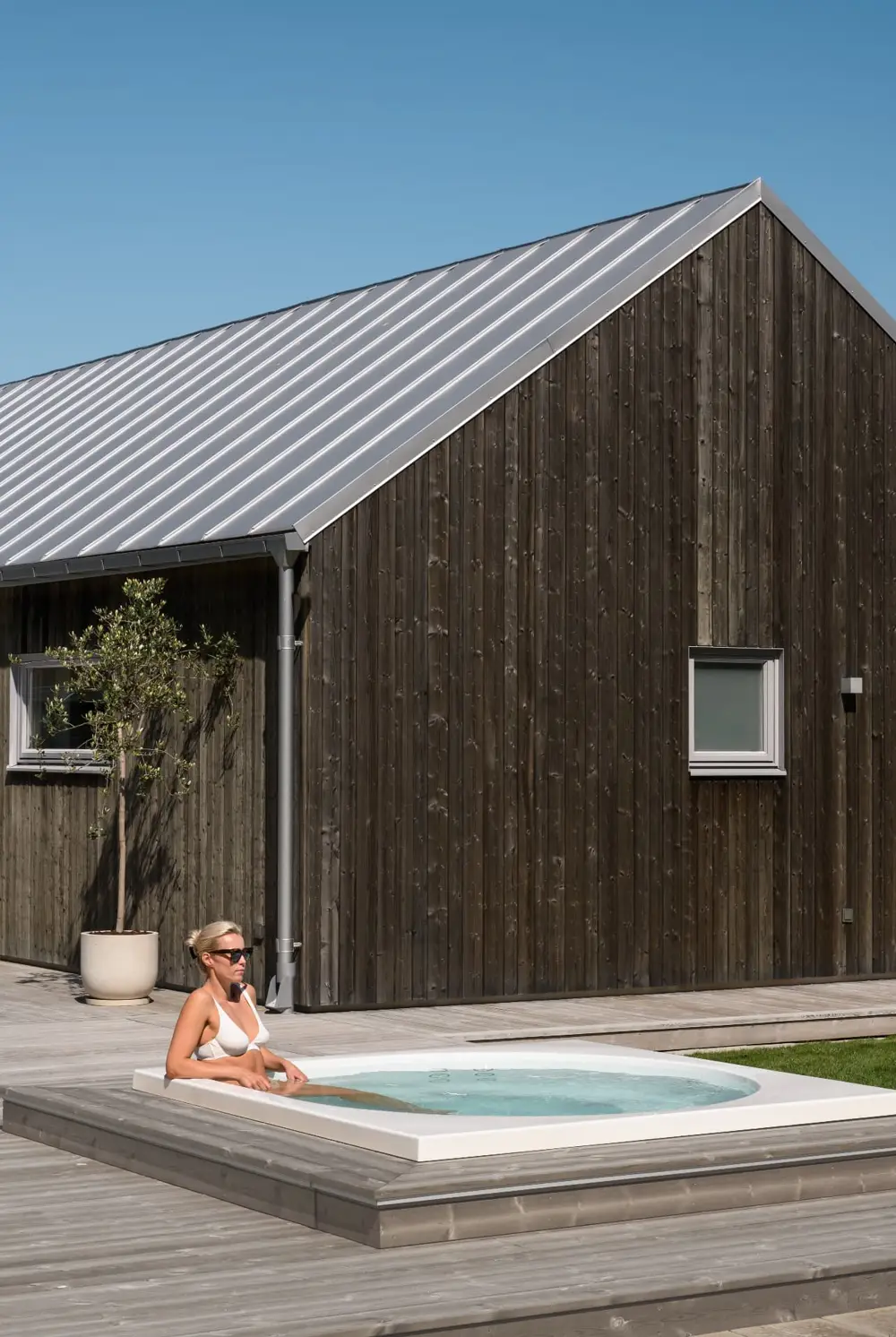 Drop Design Spa, kvinna i vitt bad vid ett svart trähus